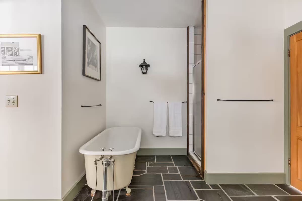 Bathroom with a vintage bathtub, a shower with glass door, and hanging towels.