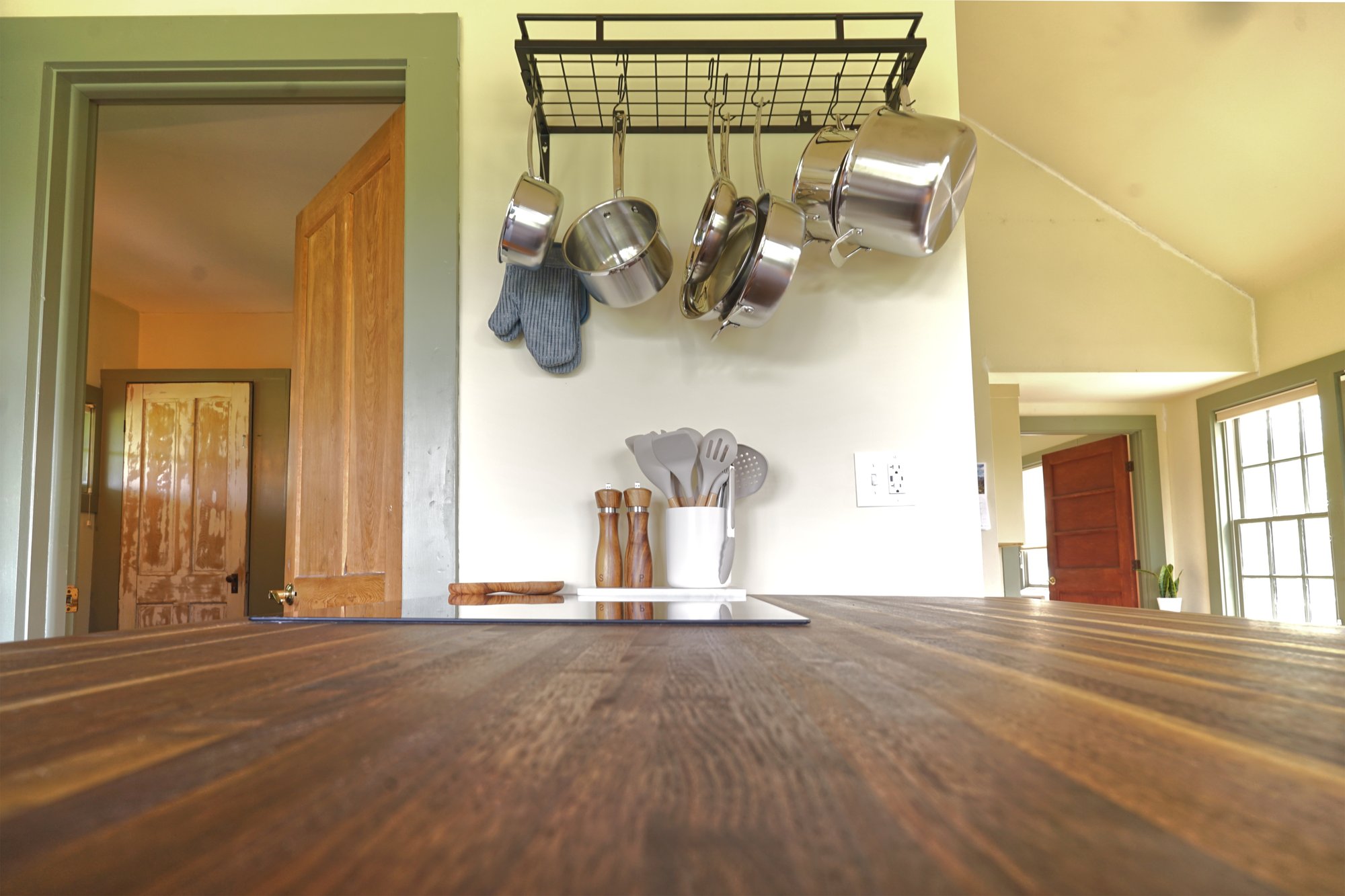 Hanging pot rack with stainless cookware above the kitchen island's wooden countertop.
