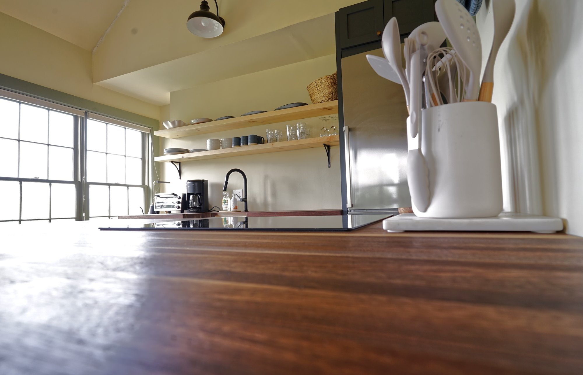 Kitchen counter with utensil crocks and cutting boards beside the refrigerator and open shelving.