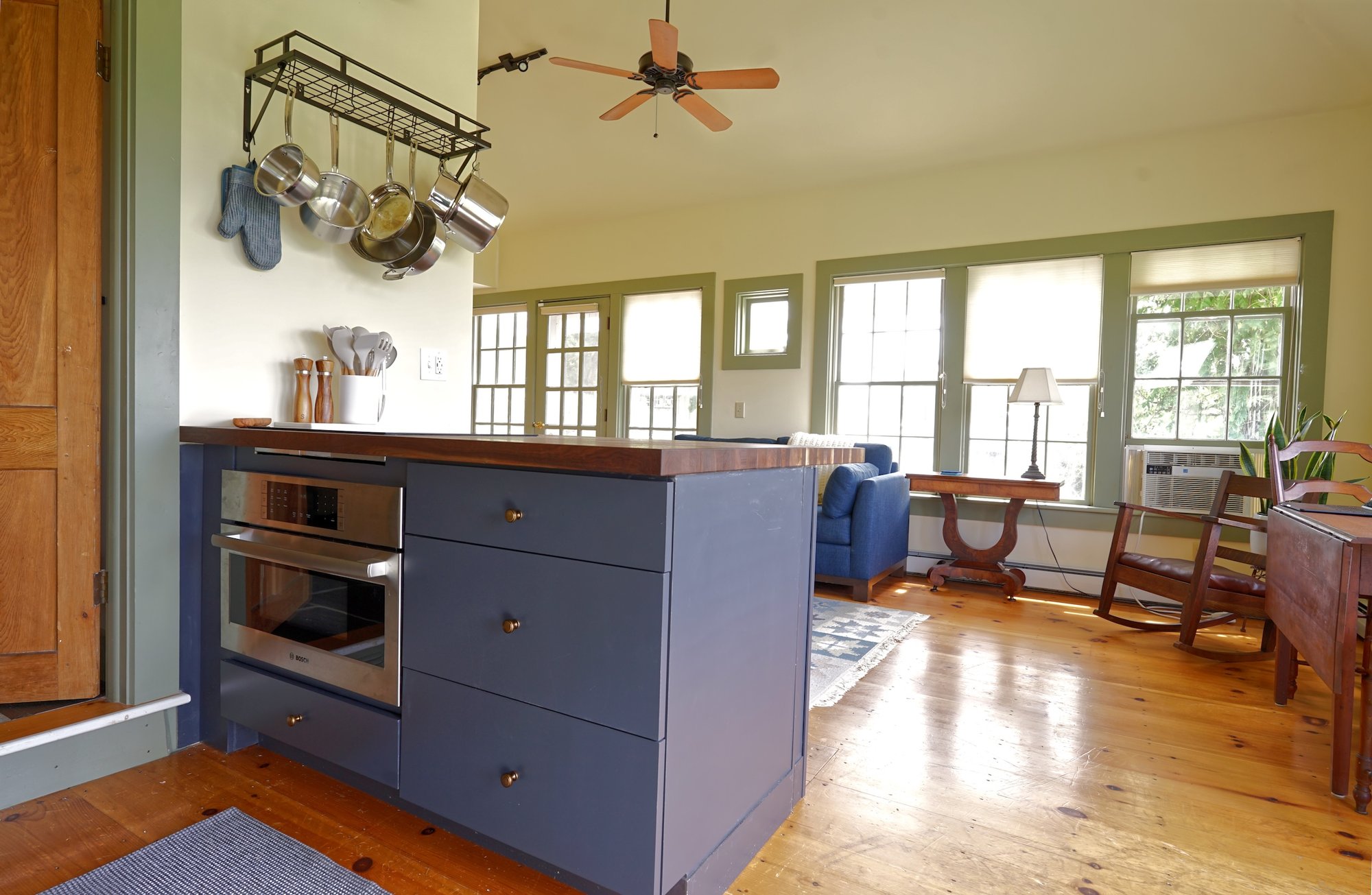 Guest house kitchen island with butcher-block countertop, induction cooktop, and built-in oven, opening to the sunlit living area.