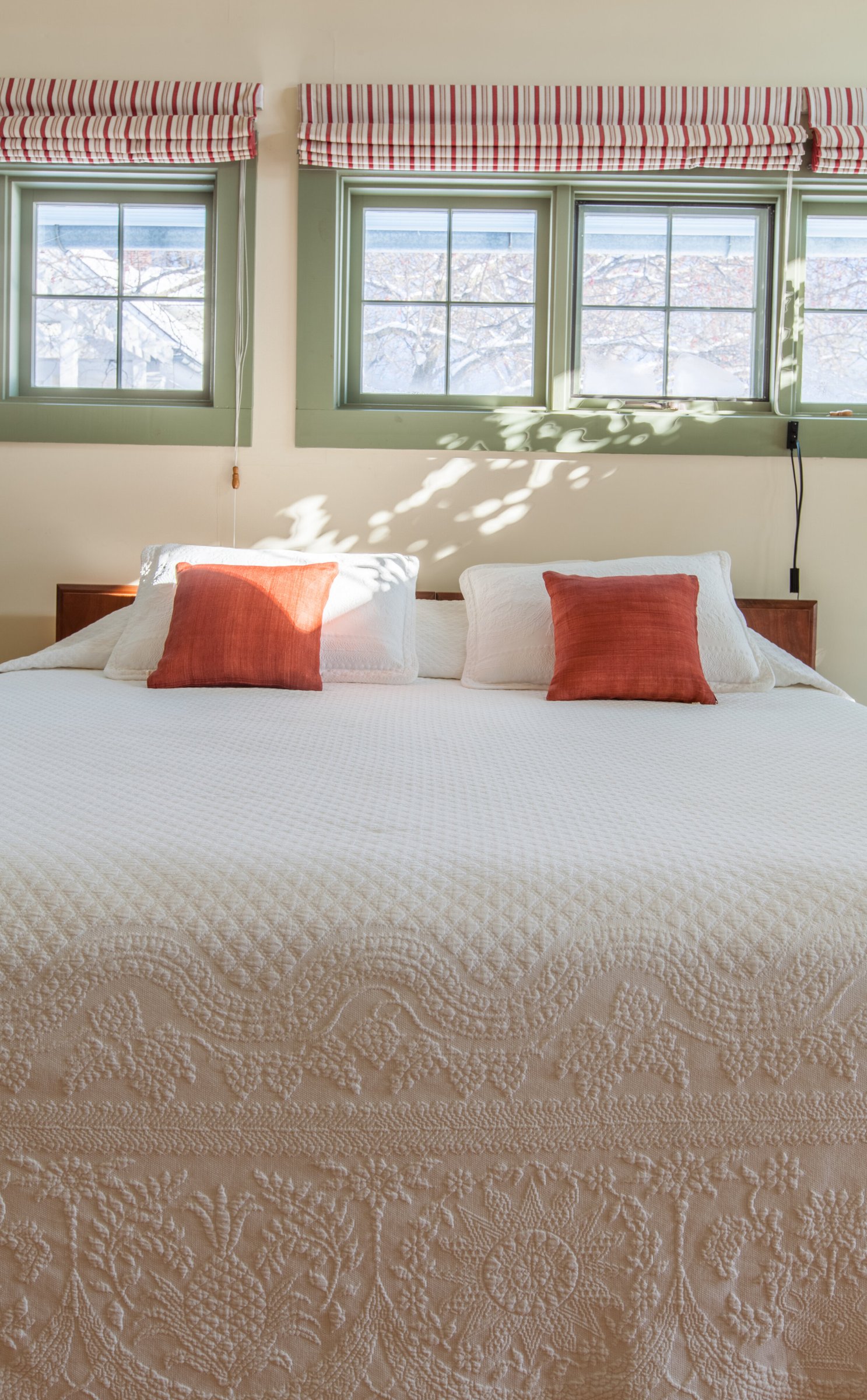 Sunlight falling across the bed's white quilt and orange accent pillows in the guest house bedroom.