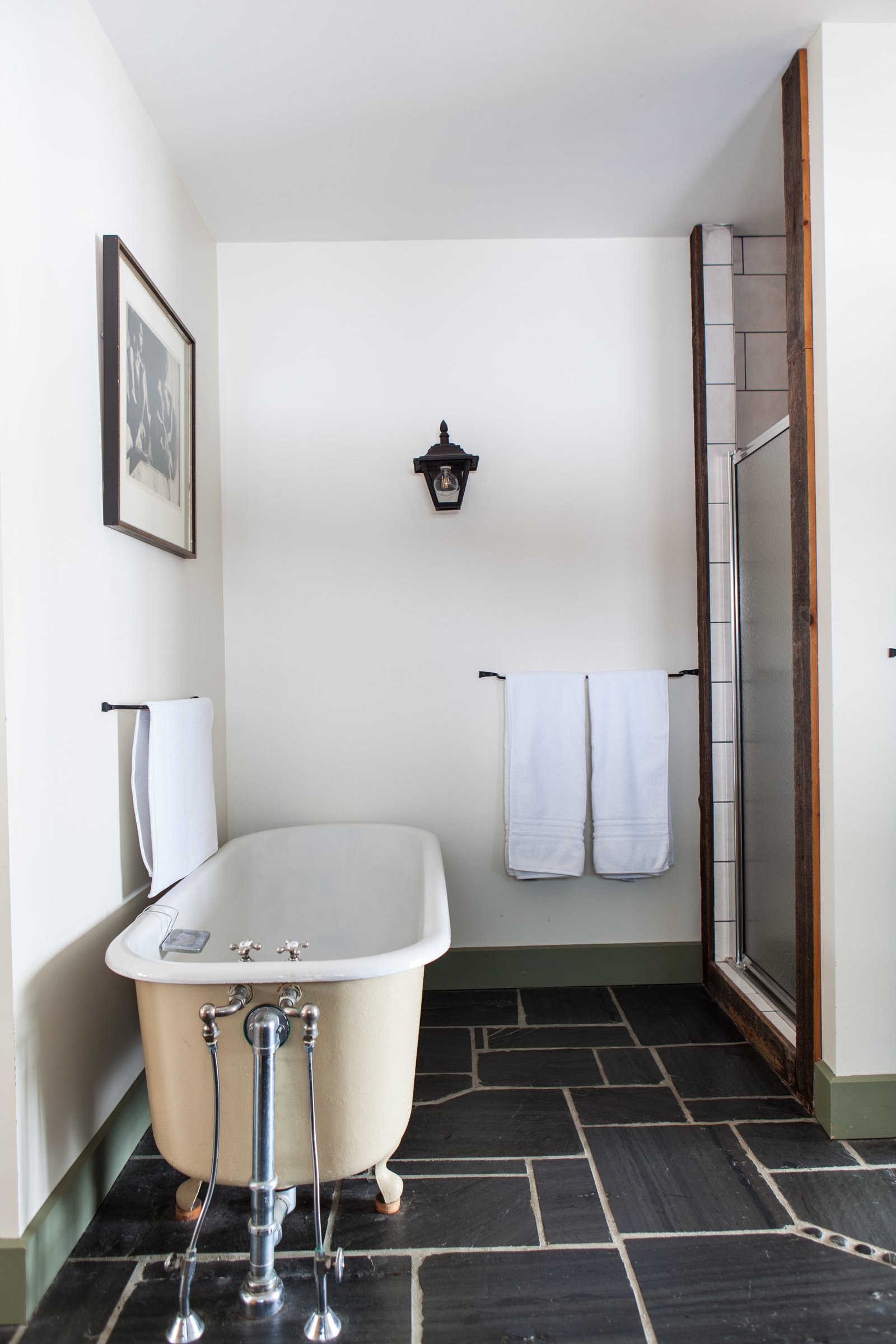 White clawfoot tub with chrome fixtures on slate tile, with fresh towels and a lantern sconce on the wall.