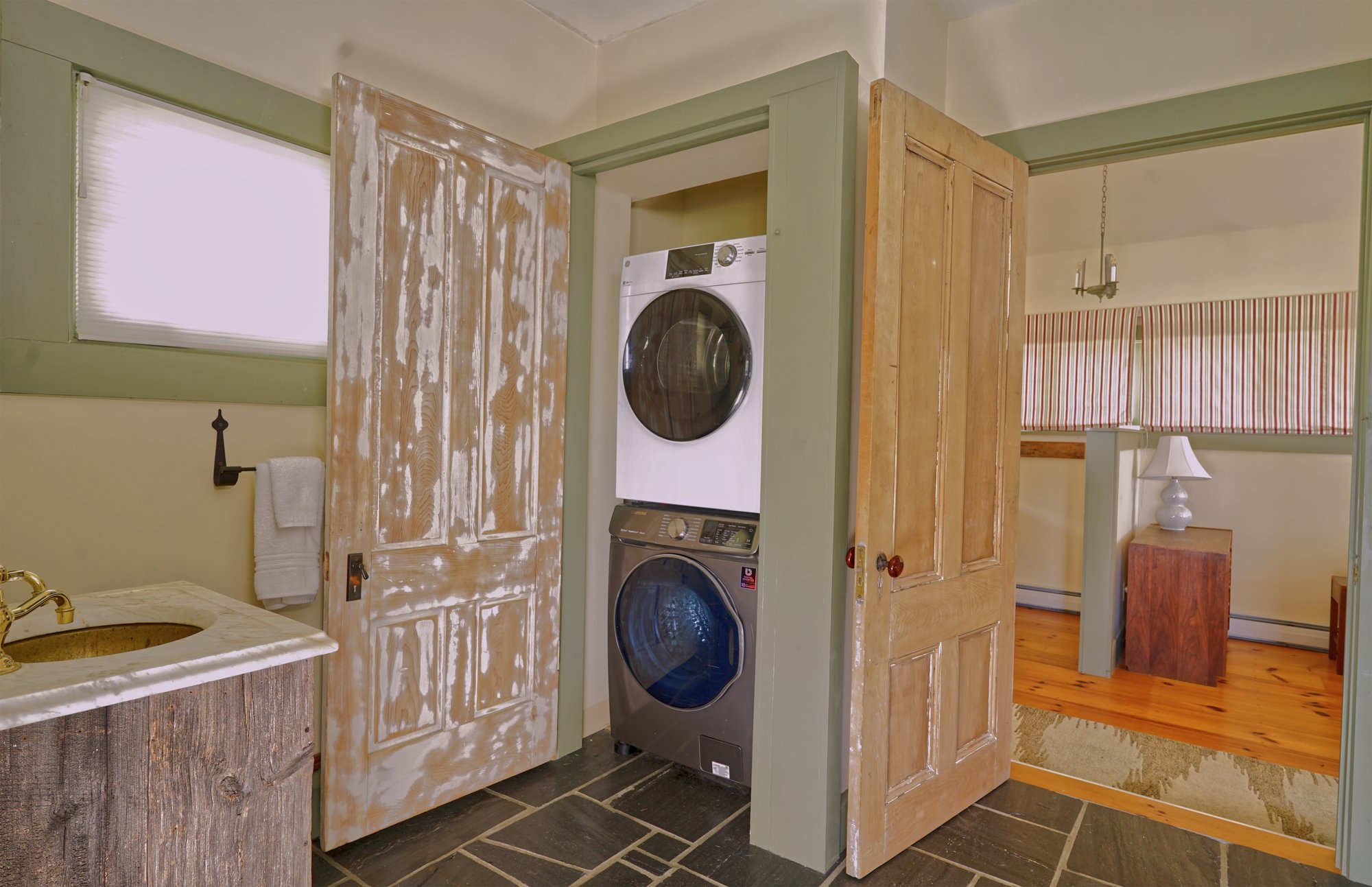 Stacked washer and dryer behind distressed antique doors beside the slate-topped laundry counter.