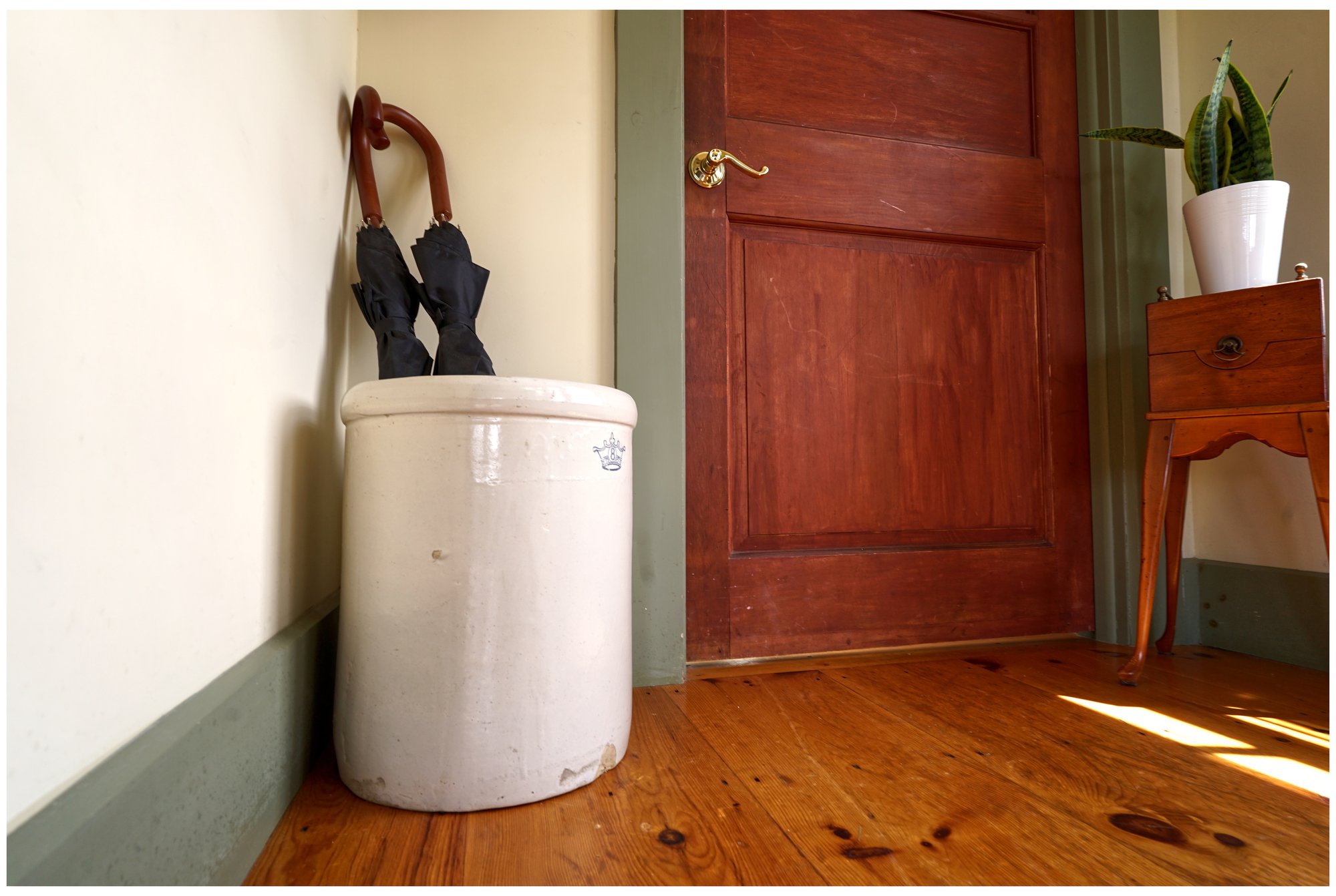 Antique stoneware crock holding umbrellas beside the guest house's wooden entry door.