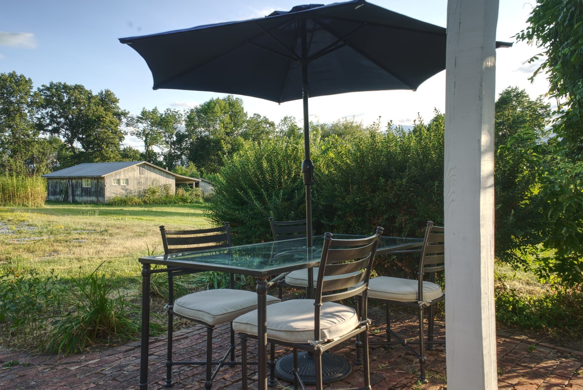 Patio dining table with umbrella on the brick terrace, looking out over the meadow toward the barn.